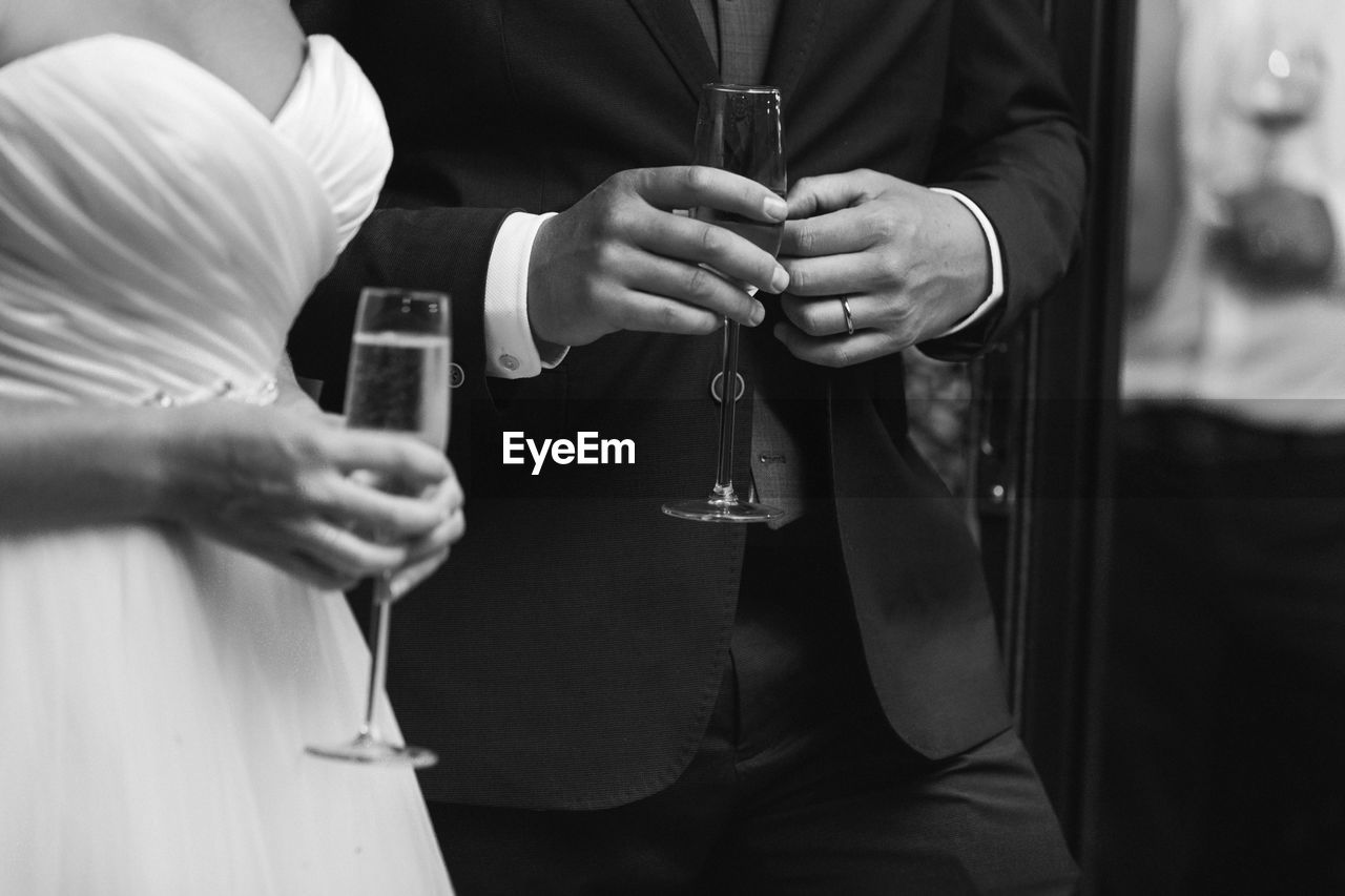 Midsection of bride and groom holding champagne flutes