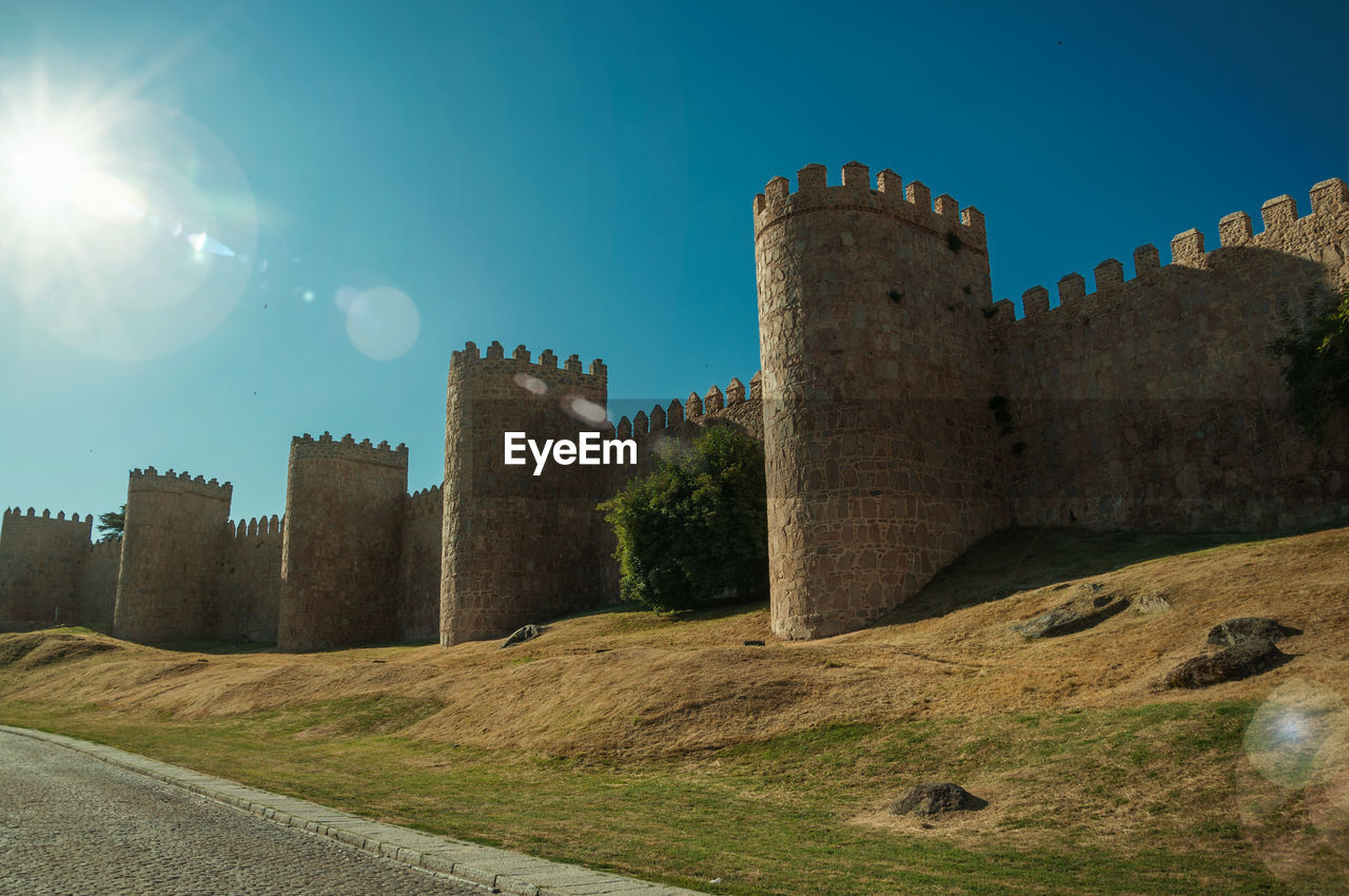 Sunbeam above lined stone towers in the large city wall and green lawn at avila, spain.