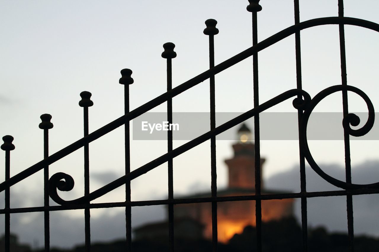 Illuminated faro di capo testa lighthouse seen through fence