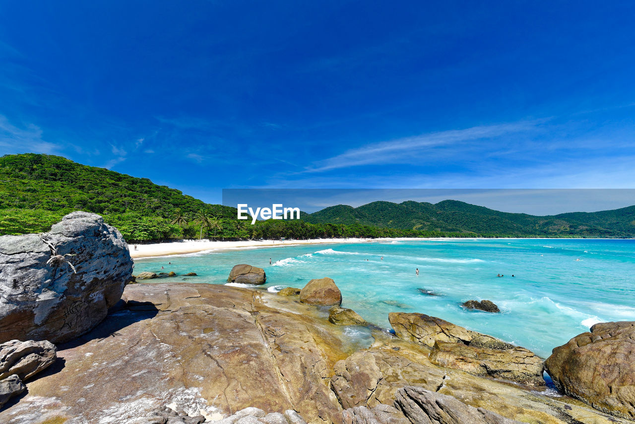 Rocks on sea shore against blue sky