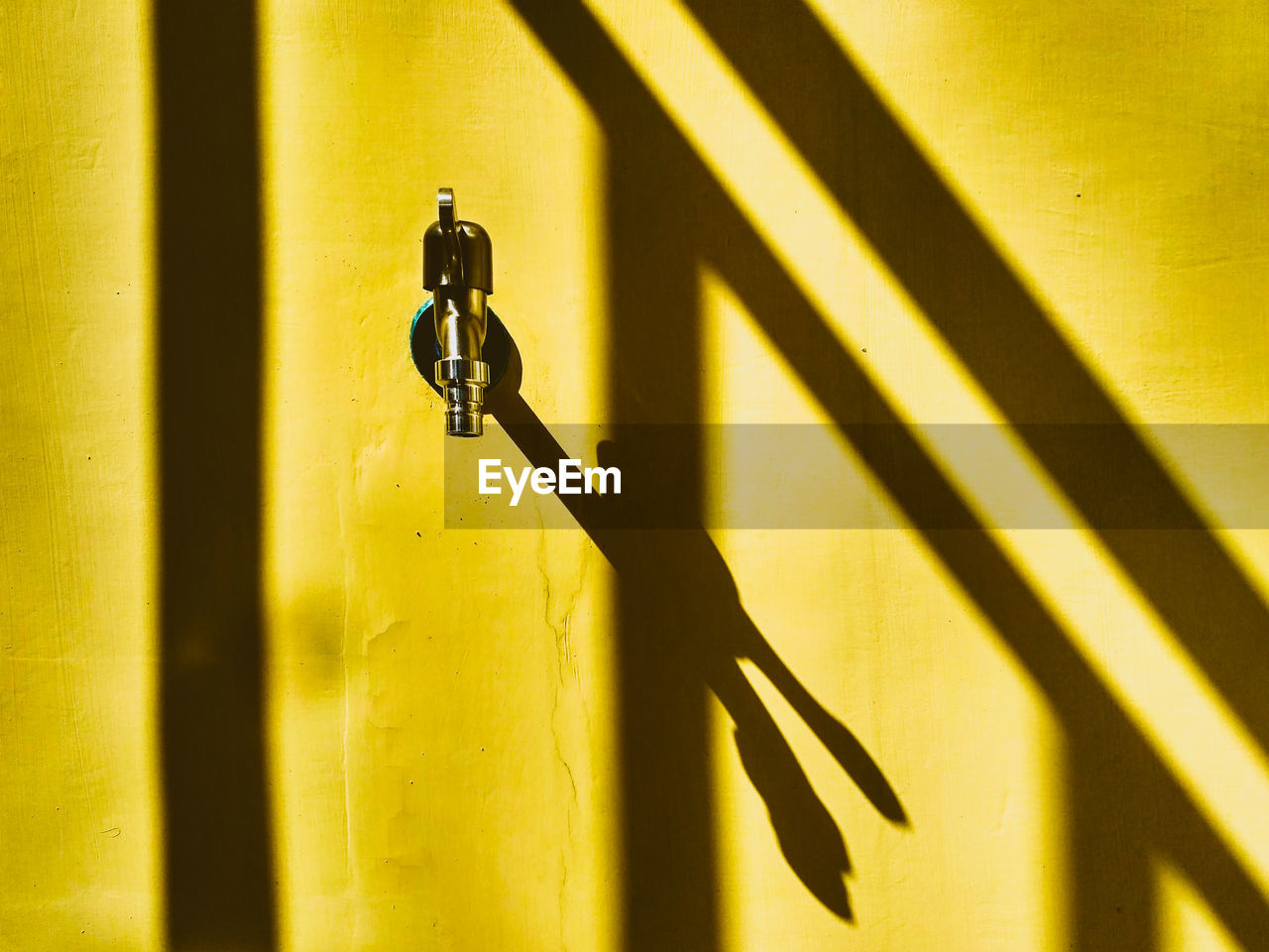 Close-up of metal faucet on yellow wall during sunny day