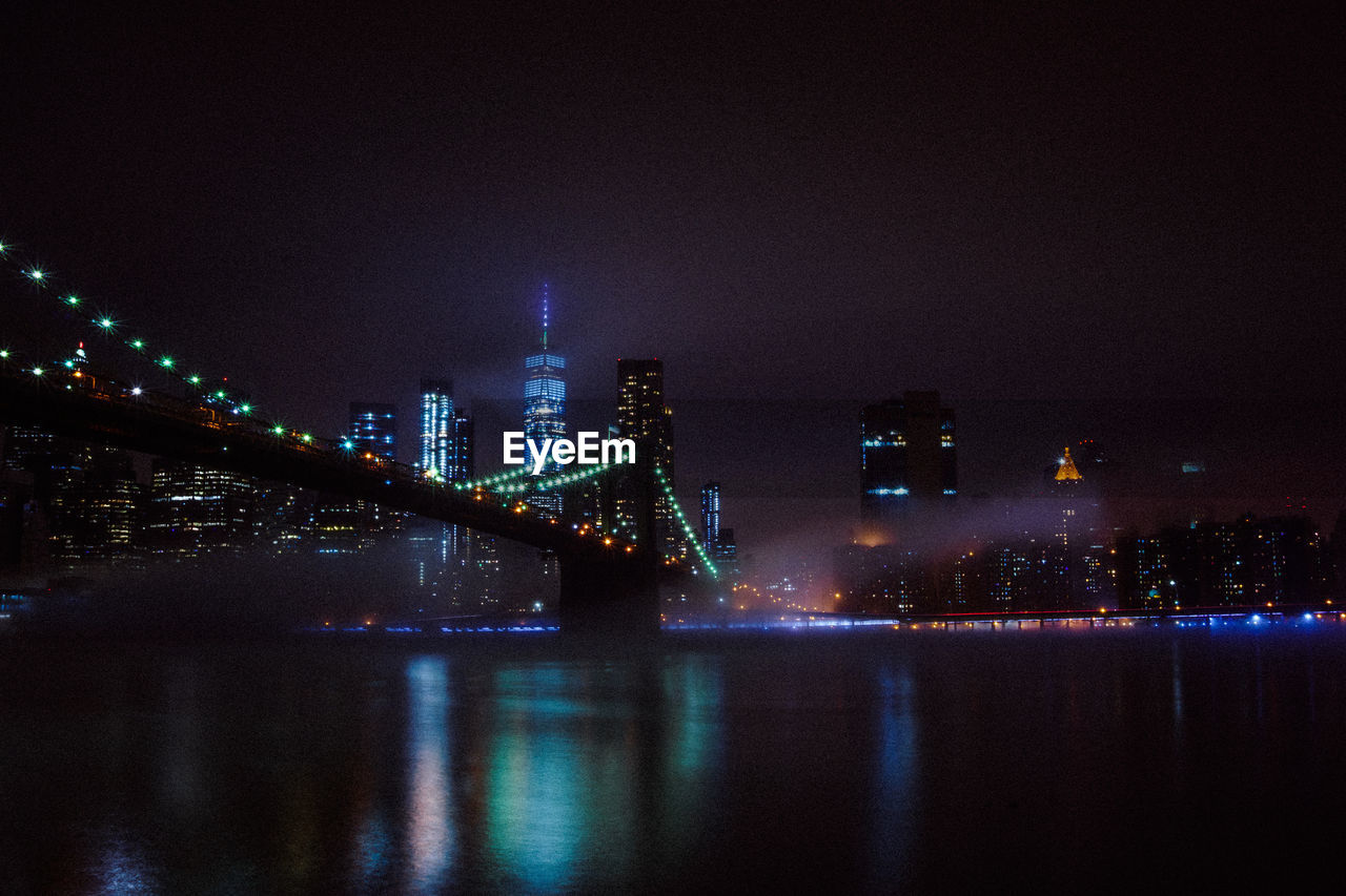 Illuminated bridge over river in city at night