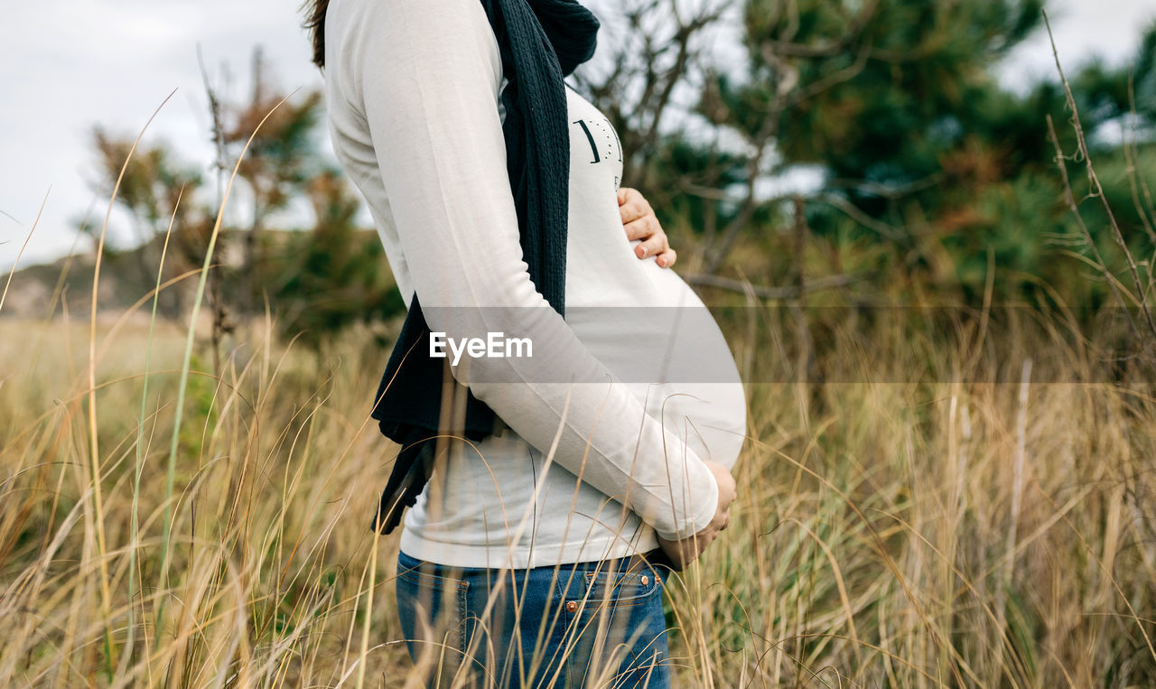 Midsection of pregnant woman standing on field