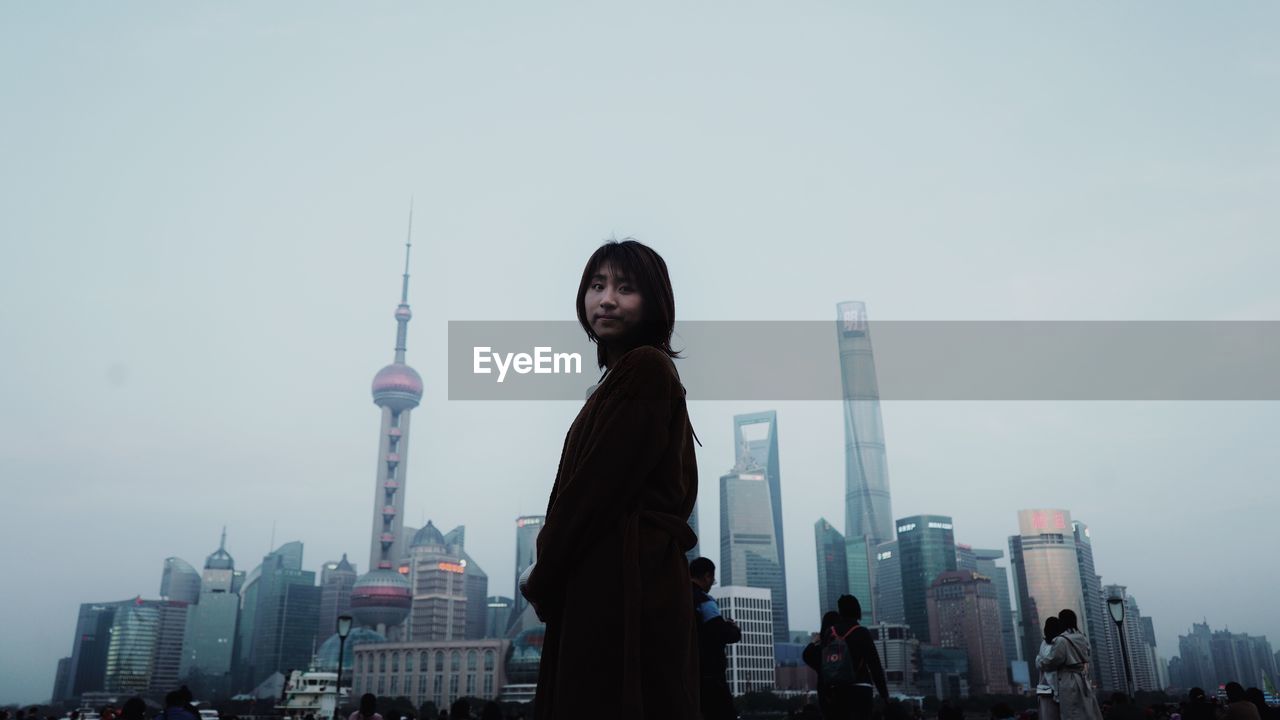 WOMAN STANDING WITH SKYSCRAPERS IN CITY