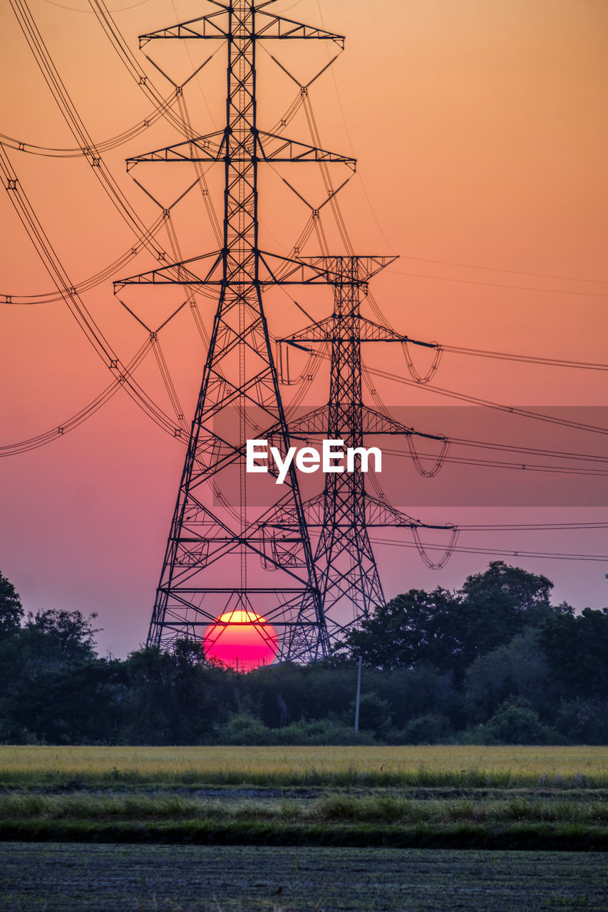 Electricity pylon substation in farmland with big red sunset for technology background