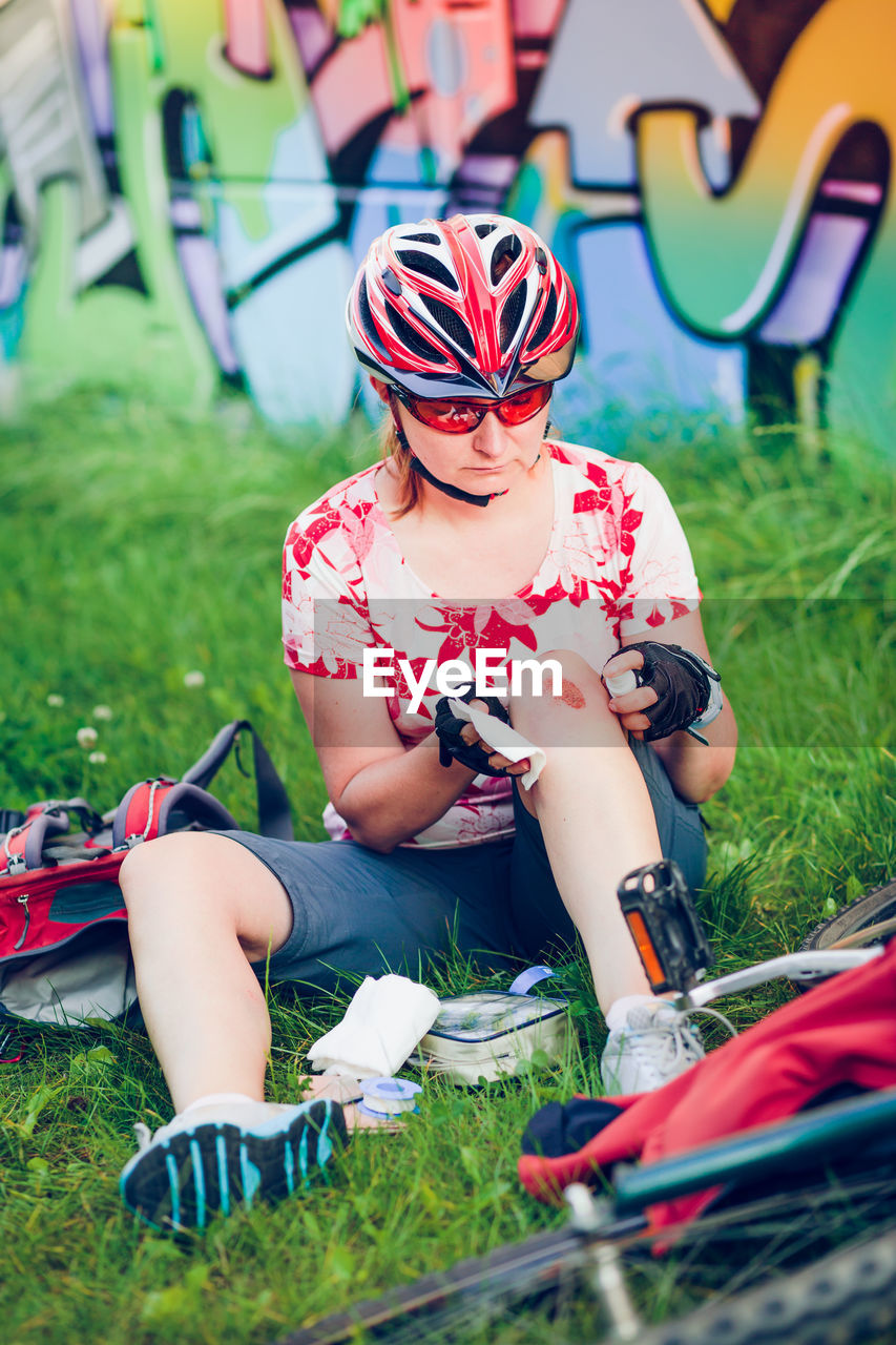 Injured female cyclist applying medicine on wound while sitting at park