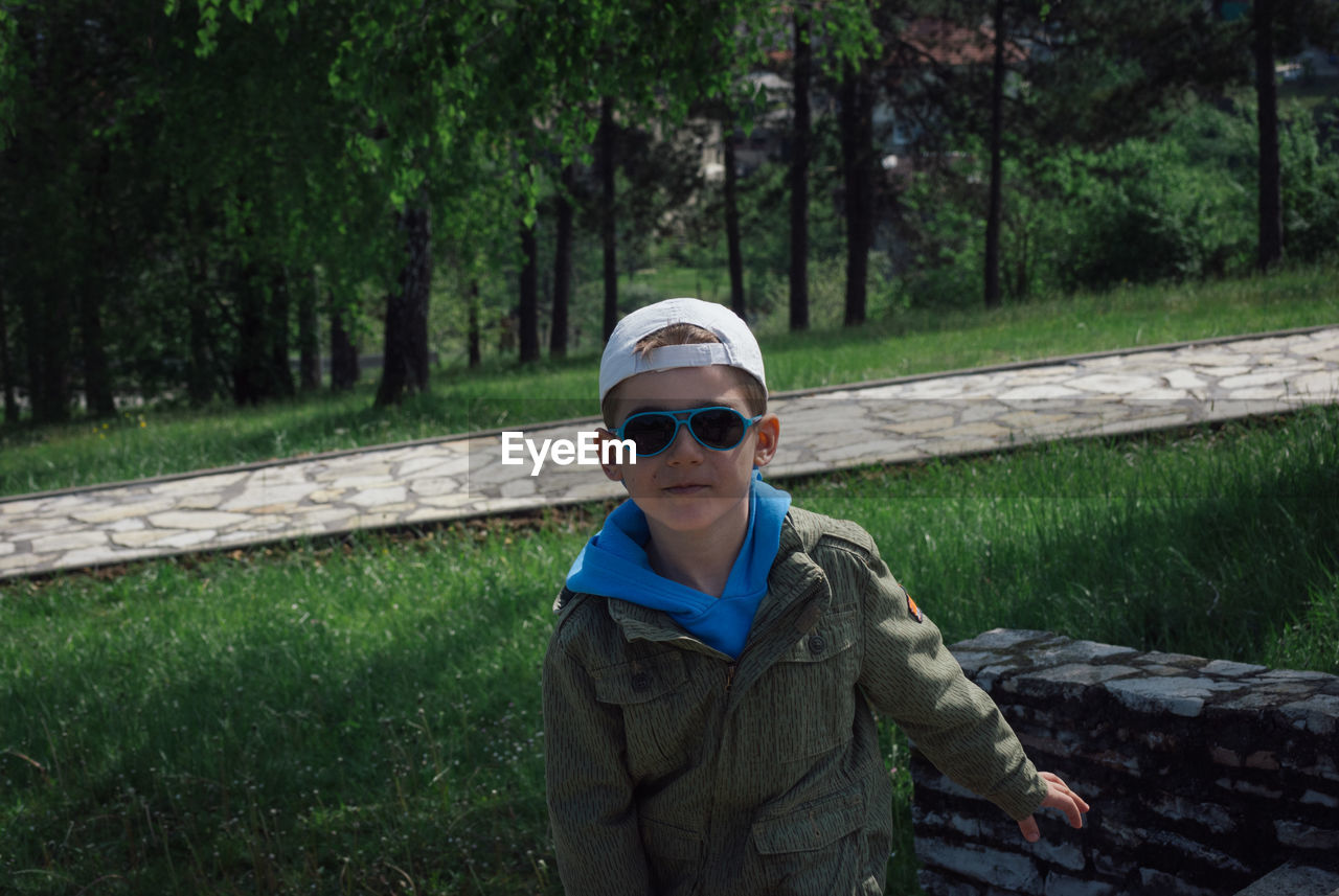 Portrait of boy in sunglasses standing on grassy field at park