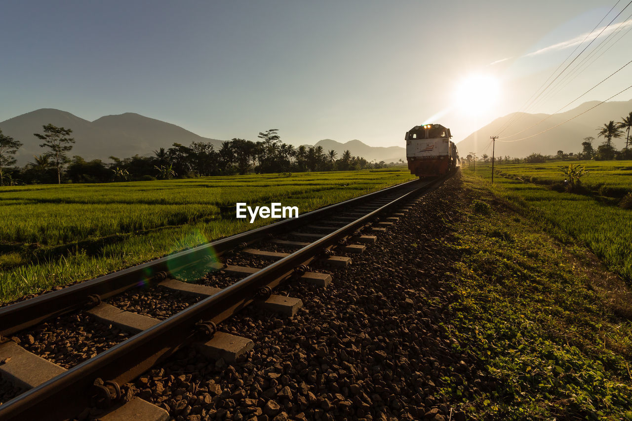 RAILROAD TRACKS ON FIELD BY MOUNTAIN AGAINST SKY