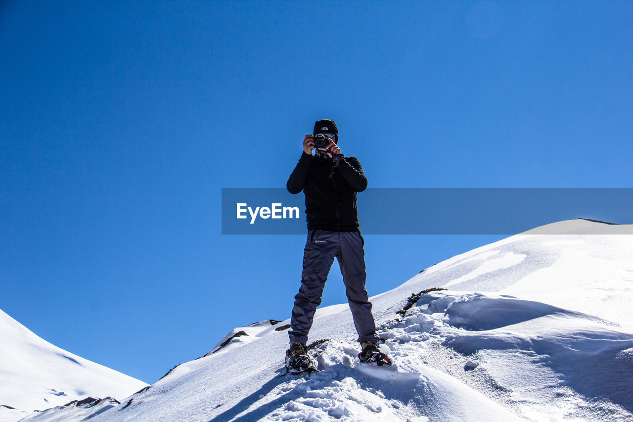 LOW ANGLE VIEW OF PERSON PHOTOGRAPHING ON MOUNTAIN