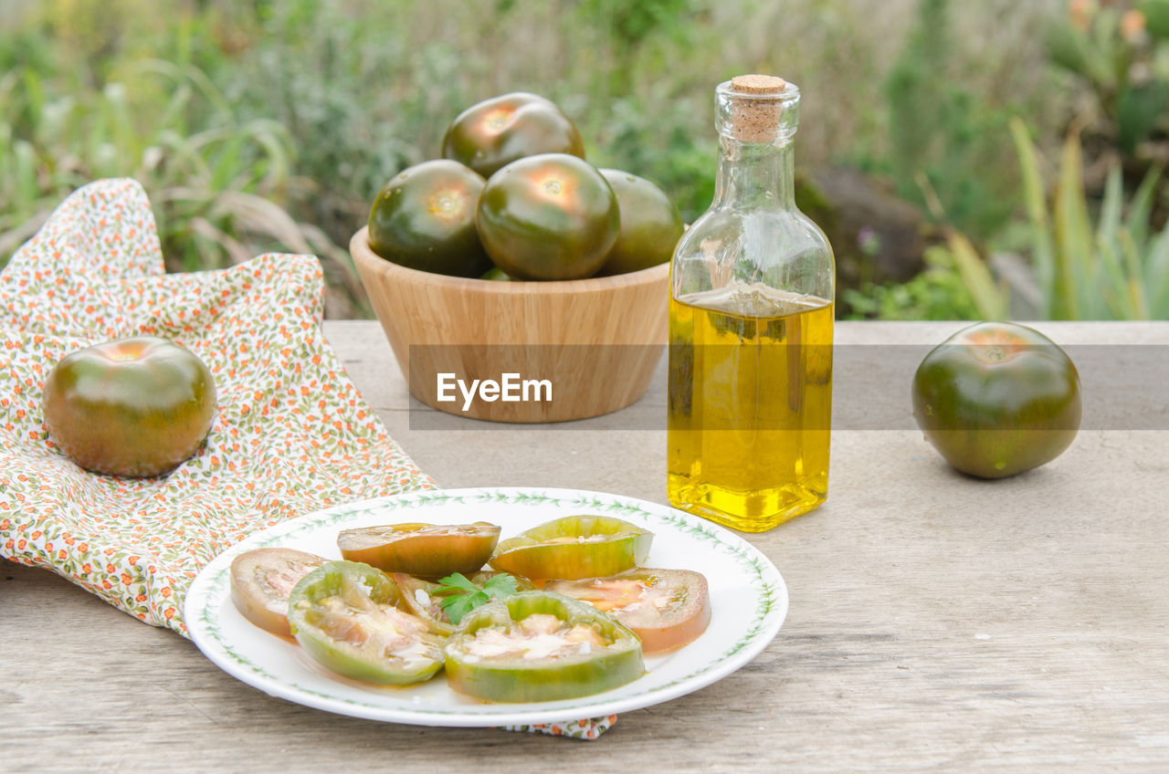 Close-up of tomato slice in plate by olive oil in bottle bowl on table