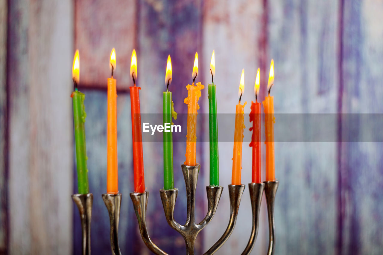 Close-up of multi colored illuminated candles against wooden wall