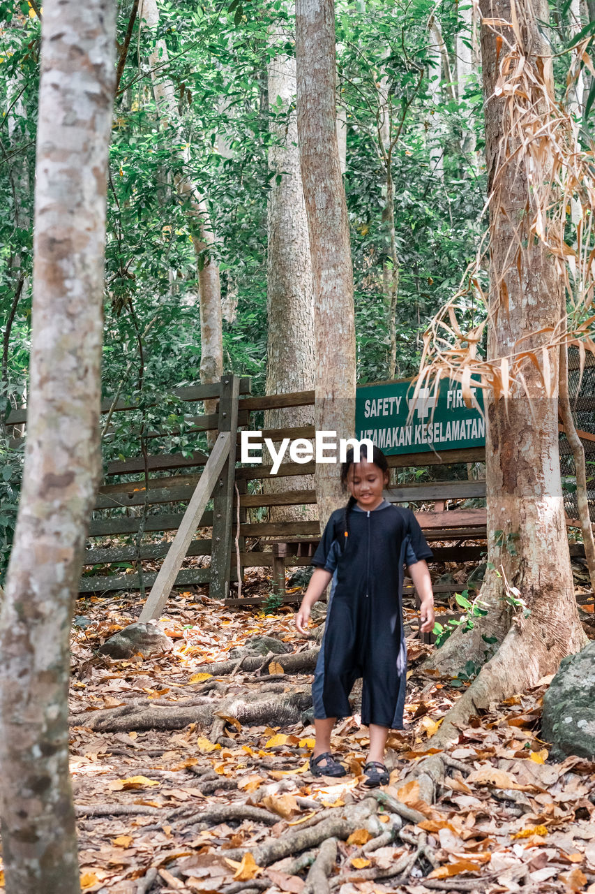 Full length of girl standing on land against tree trunk in forest