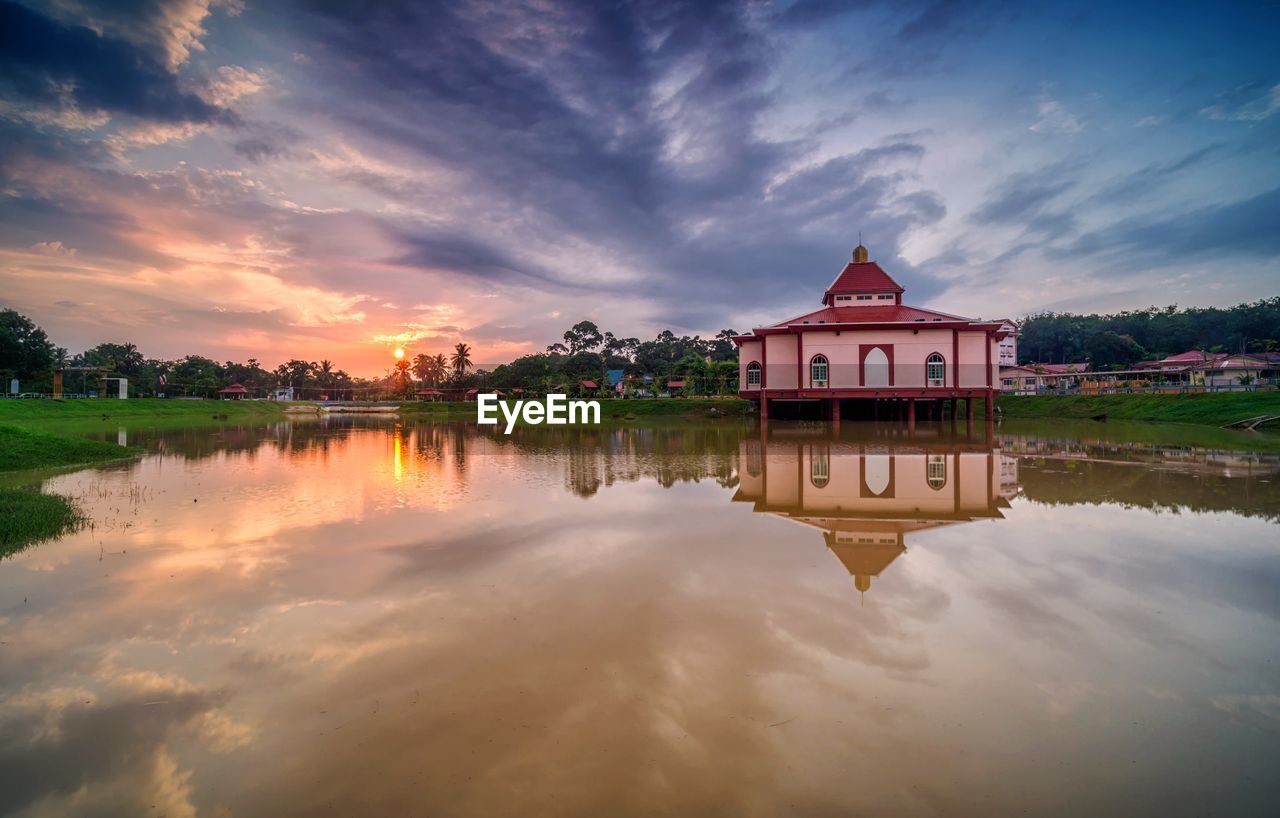 REFLECTION OF BUILDING ON LAKE AT SUNSET