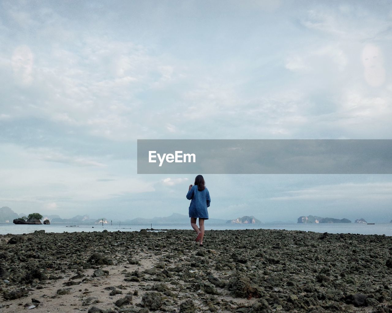 Rear view of woman standing on beach against sky