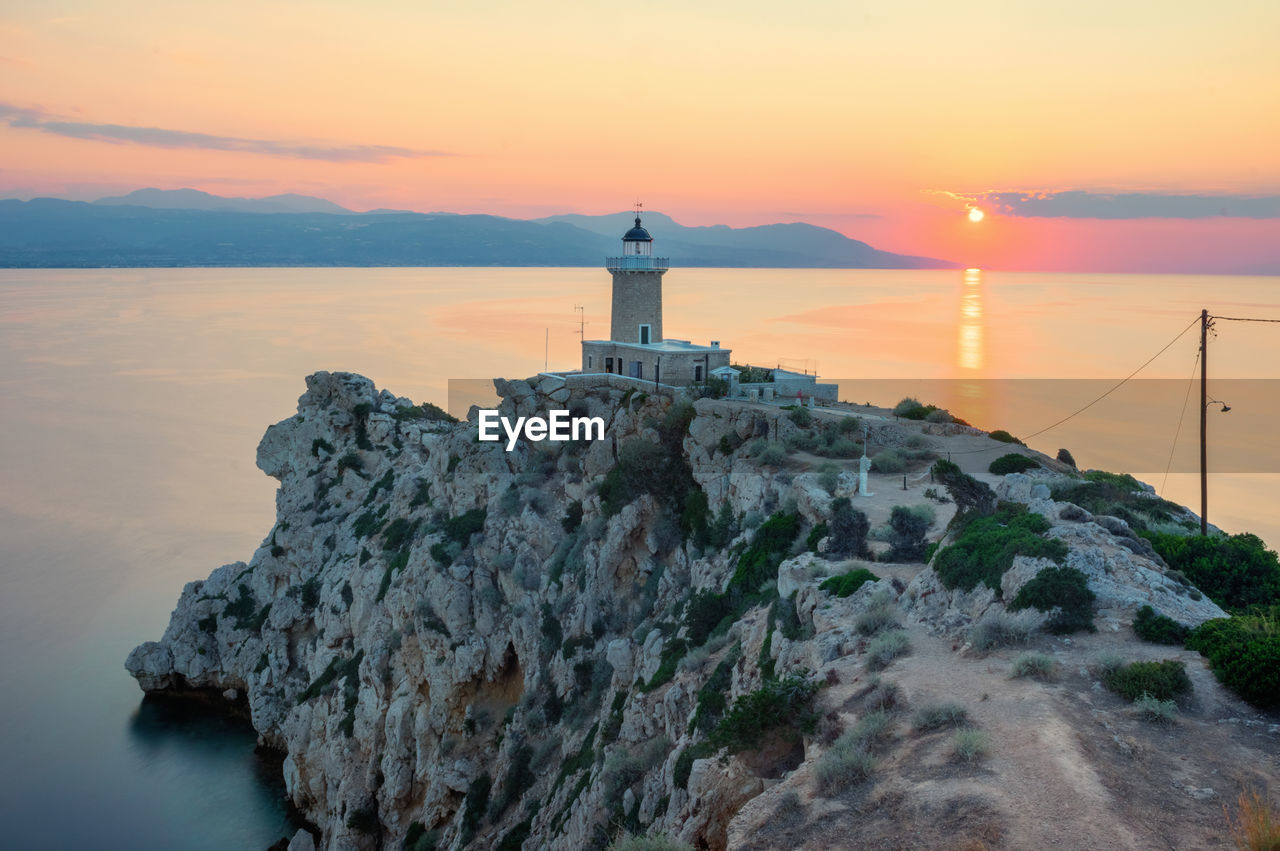 Lighthouse by sea against sky during sunset