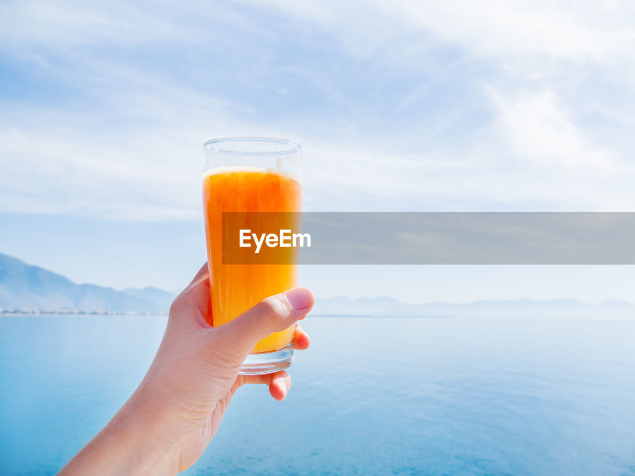 Hand with fresh tasty freshly-squeezed juice of ripe oranges in glass. seascape. kemer, turkey.