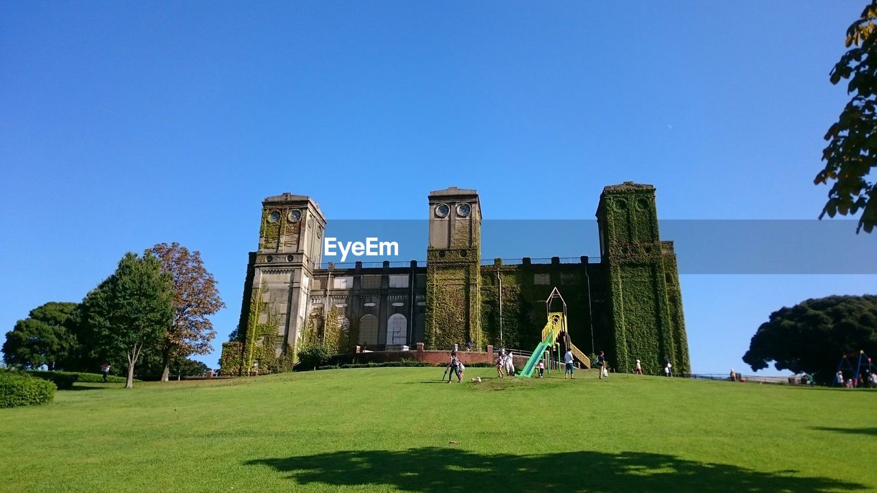 PEOPLE SITTING ON GRASSY LANDSCAPE AGAINST BLUE SKY