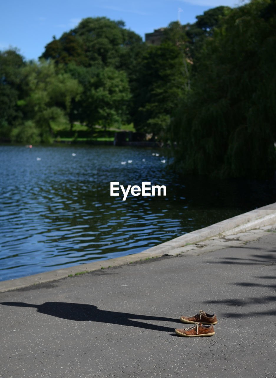 Shadow of man with shoes on footpath by lake