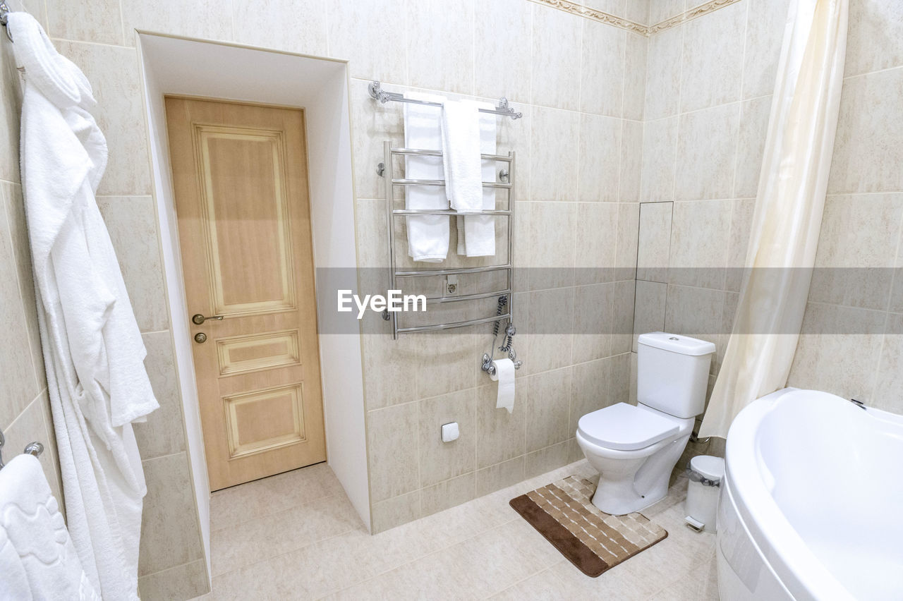 Bathroom with white sink and toilet. white bathrobes for guests hang on the wall.