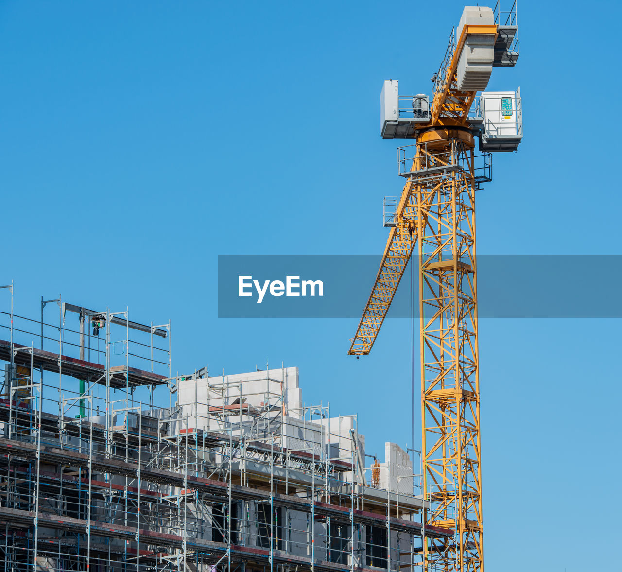 Low angle view of crane by incomplete building against clear blue sky