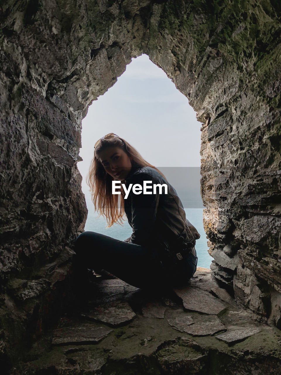 Portrait of woman sitting in old rocky window by sea