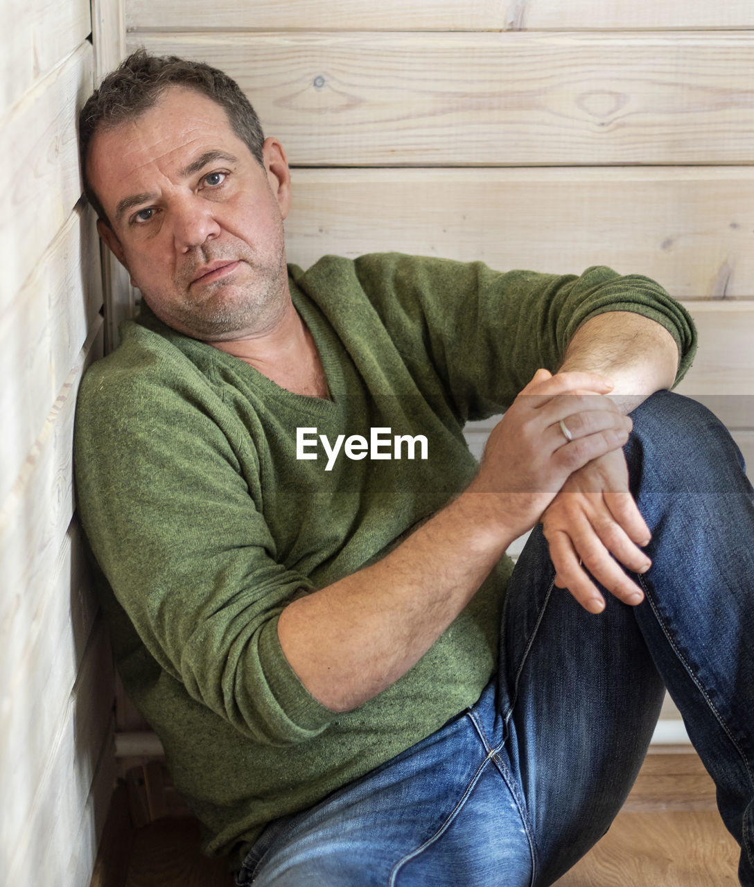 Portrait of depressed mature man sitting on hardwood floor at home