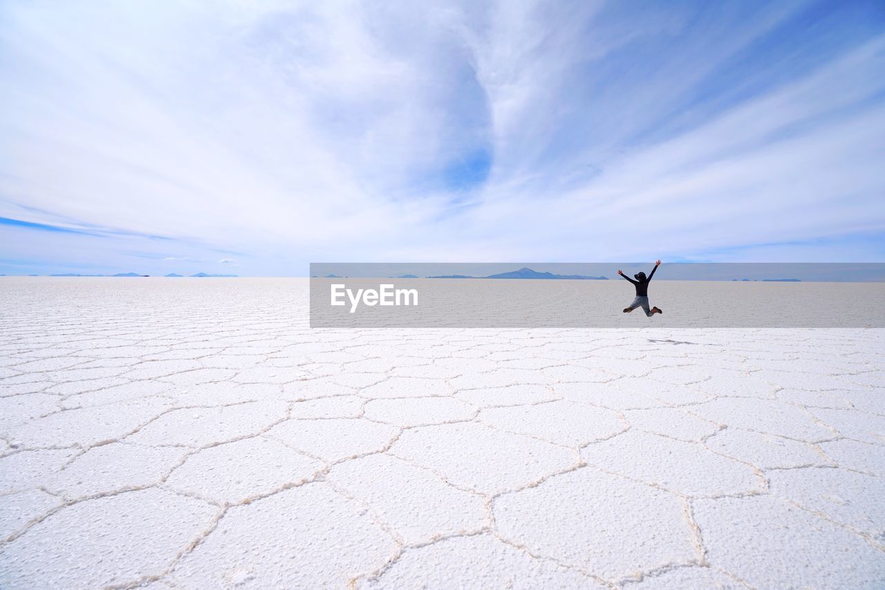 Full length of woman jumping at salt desert against sky