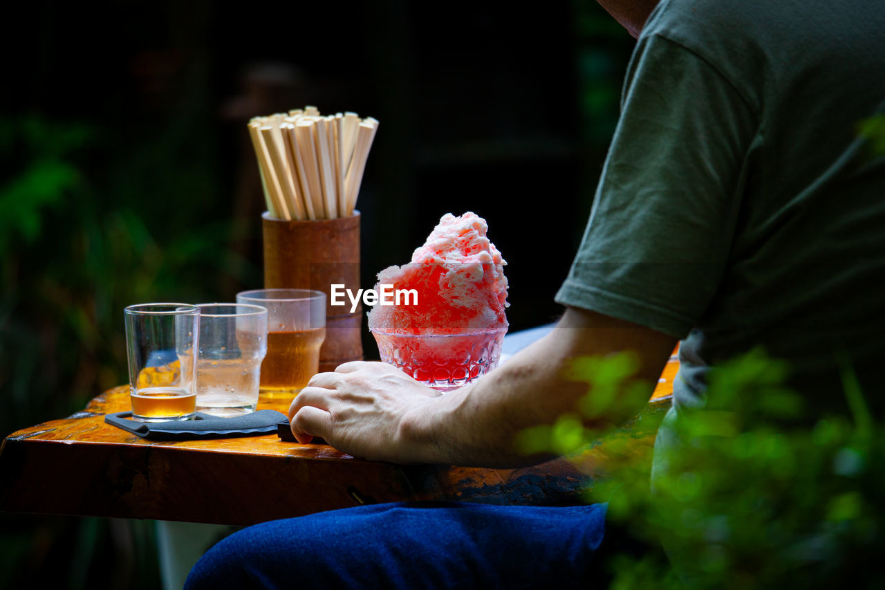 Midsection of man eating kakigoori sitting on table