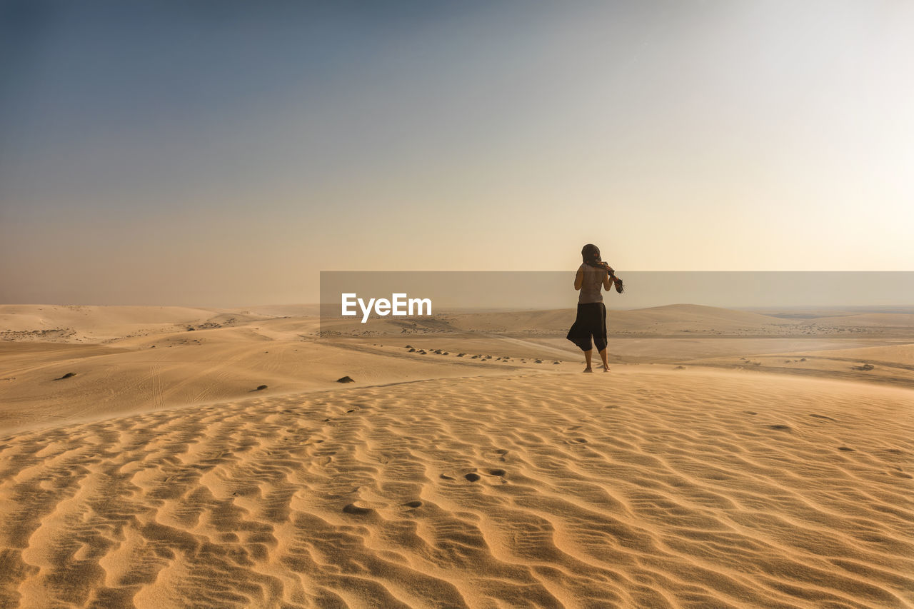 Rear view of woman walking on sand at beach against clear sky