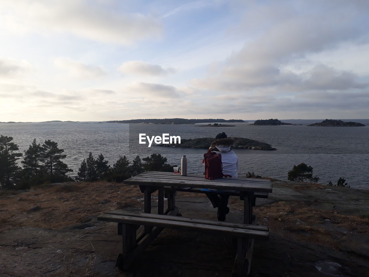 REAR VIEW OF MAN ON TABLE BY SEA