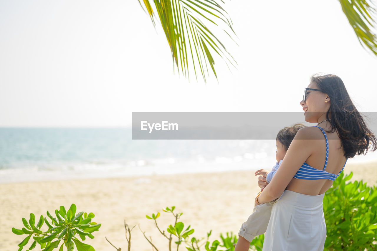 Mother with son standing at beach against sky