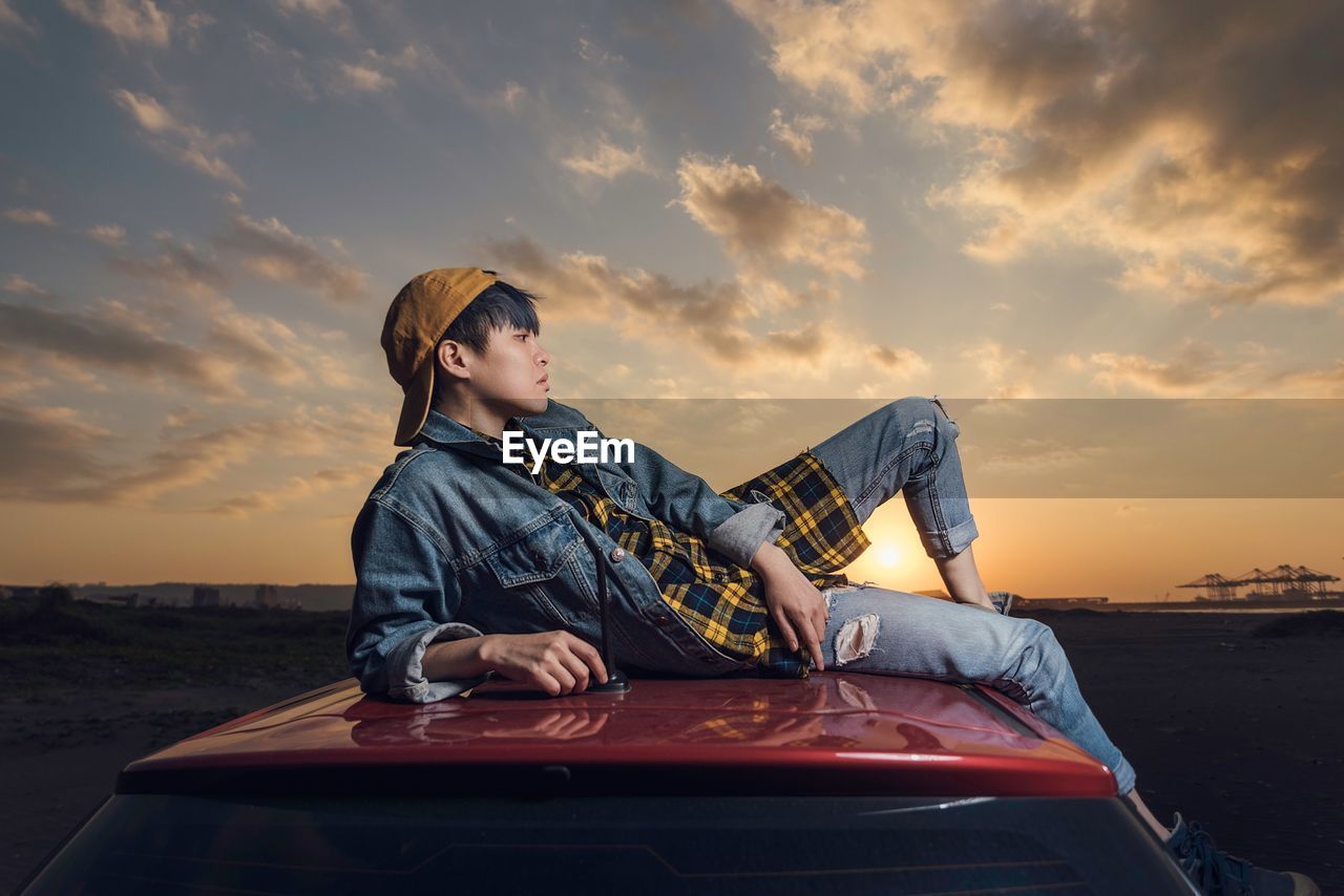 BOY STANDING ON BOAT AGAINST SKY AT SUNSET