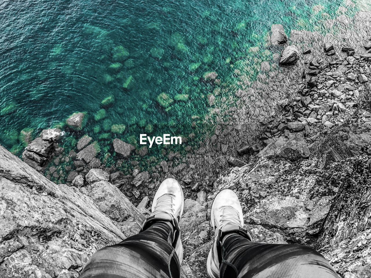 Low section of man sitting on rock by sea