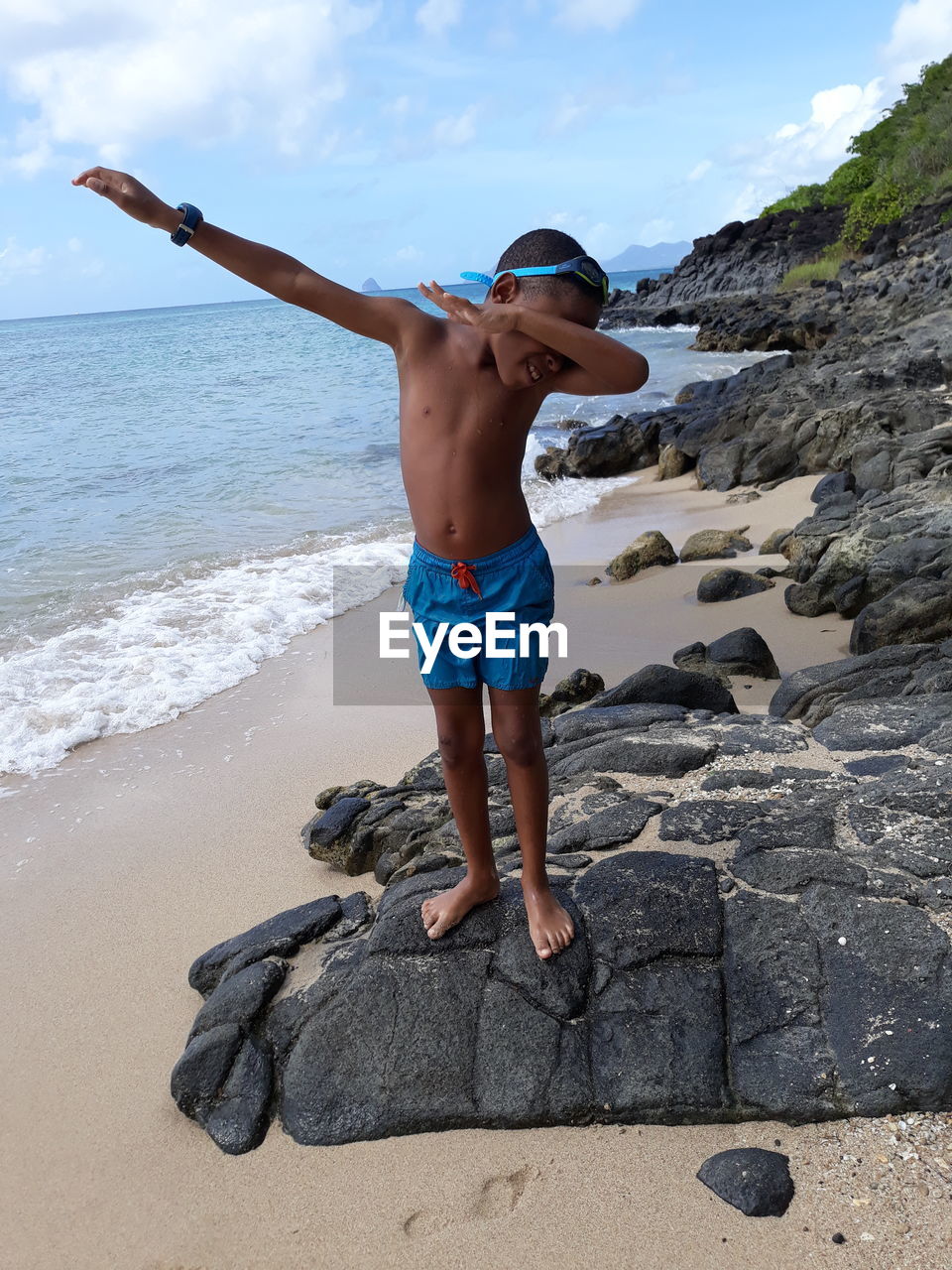 Full length of shirtless boy gesturing while standing on rocks at beach