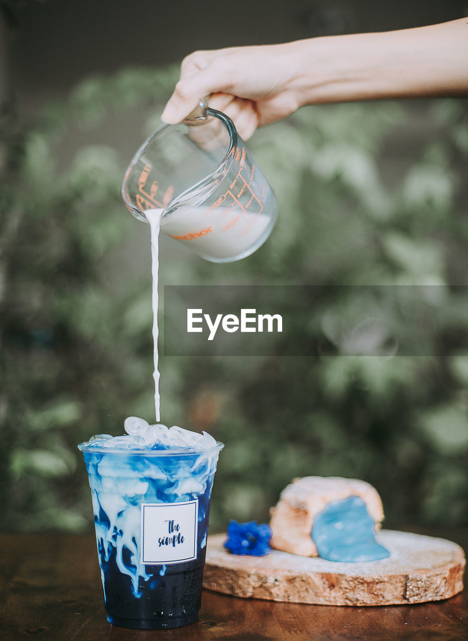 Cropped hand of woman pouring milk in drink outdoors