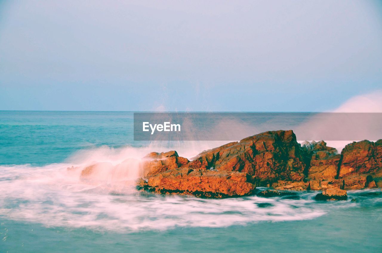 Scenic view of waves crashing on rocks against sky