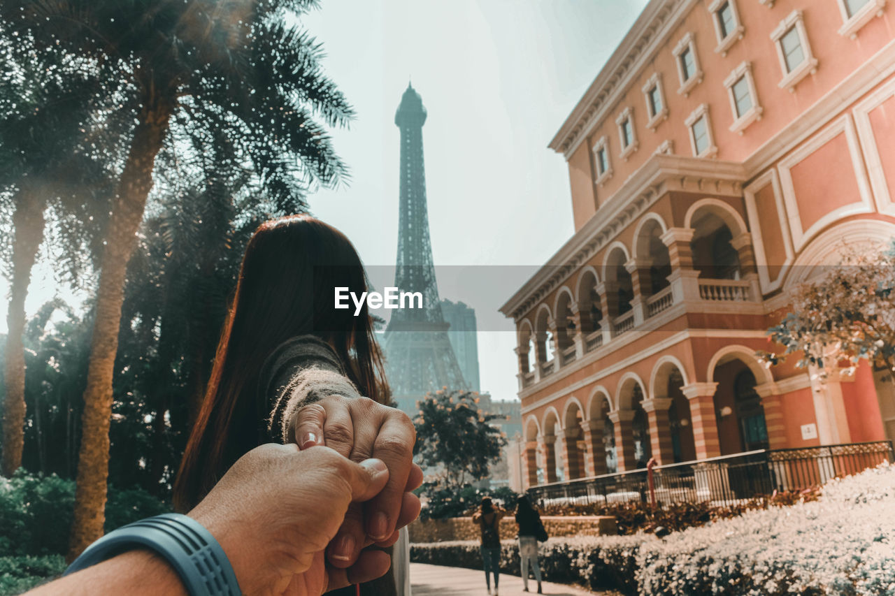 Cropped image of man holding girlfriend hand against building