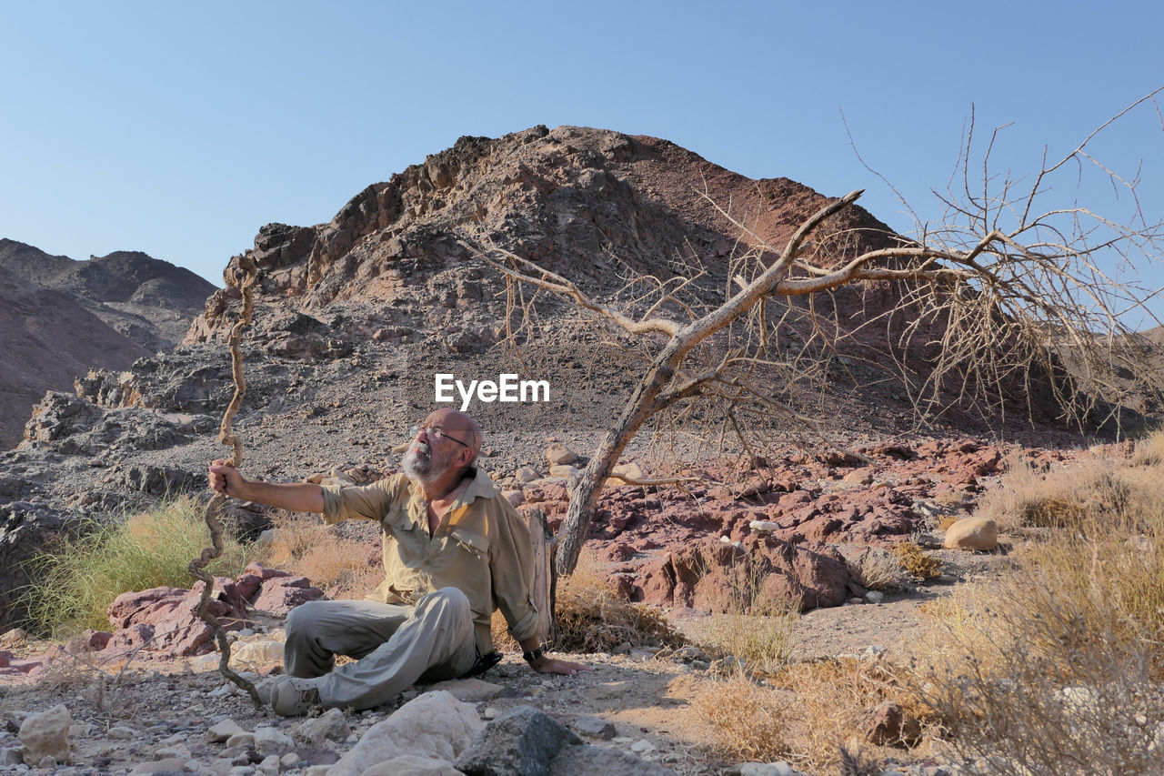 Senior man sitting on rock against sky in the desert 