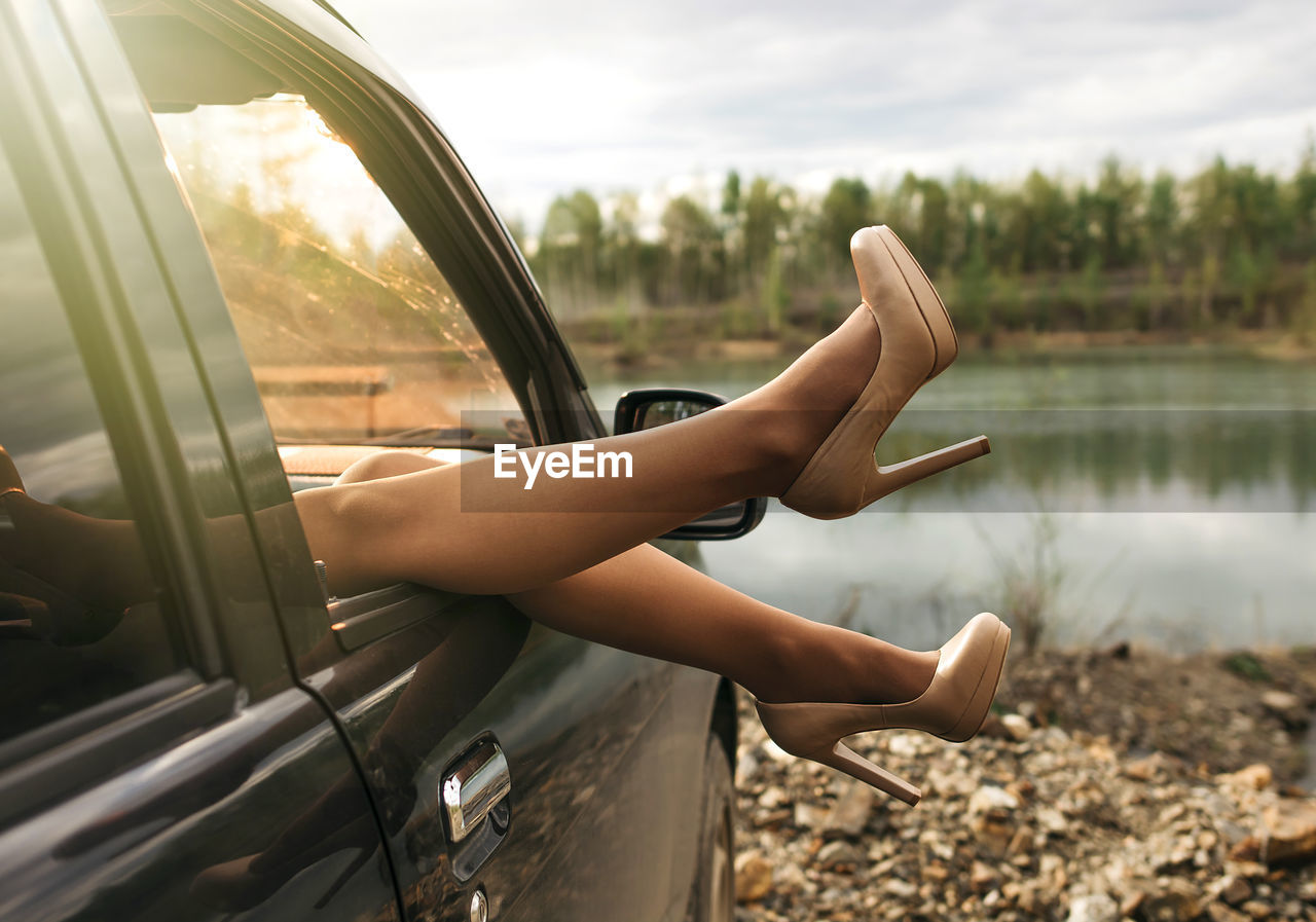 Low section of woman in car against lake and sky