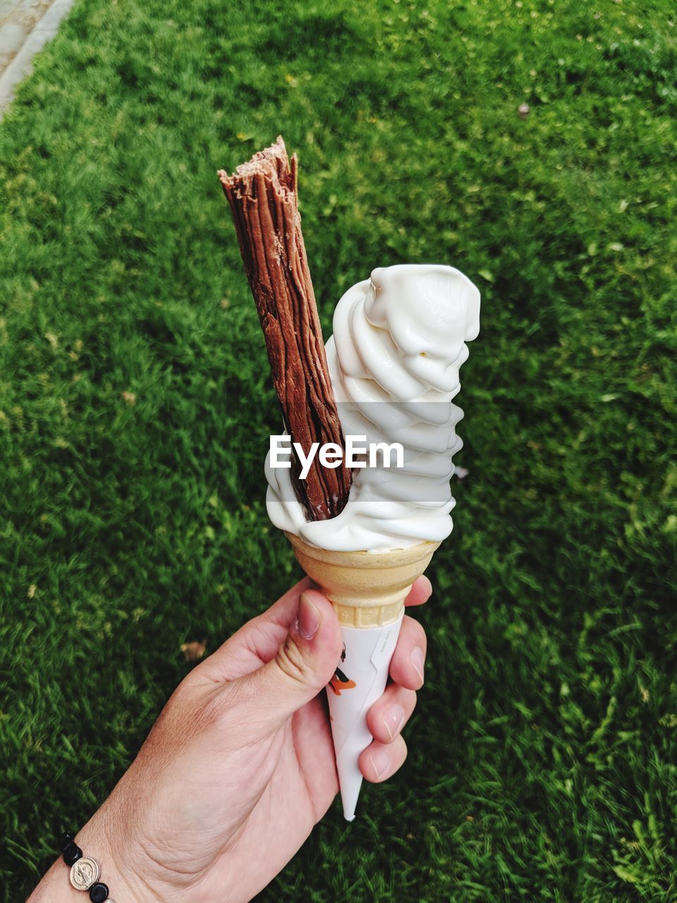 CLOSE-UP OF HAND HOLDING ICE CREAM CONE AGAINST TREES