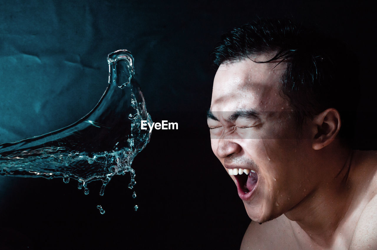 Close-up of shirtless man making face by water against black background