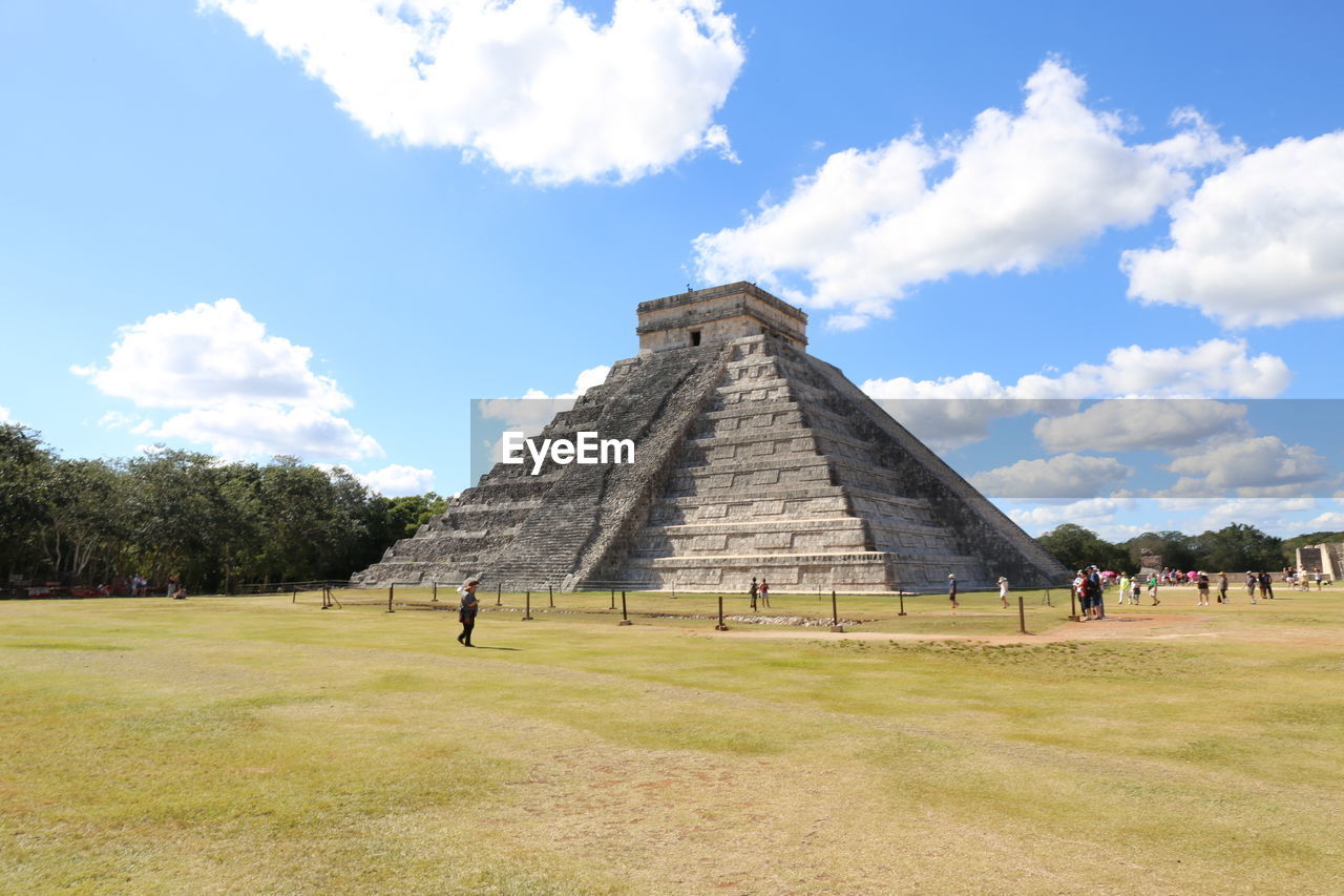 Tourists on field against cloudy sky