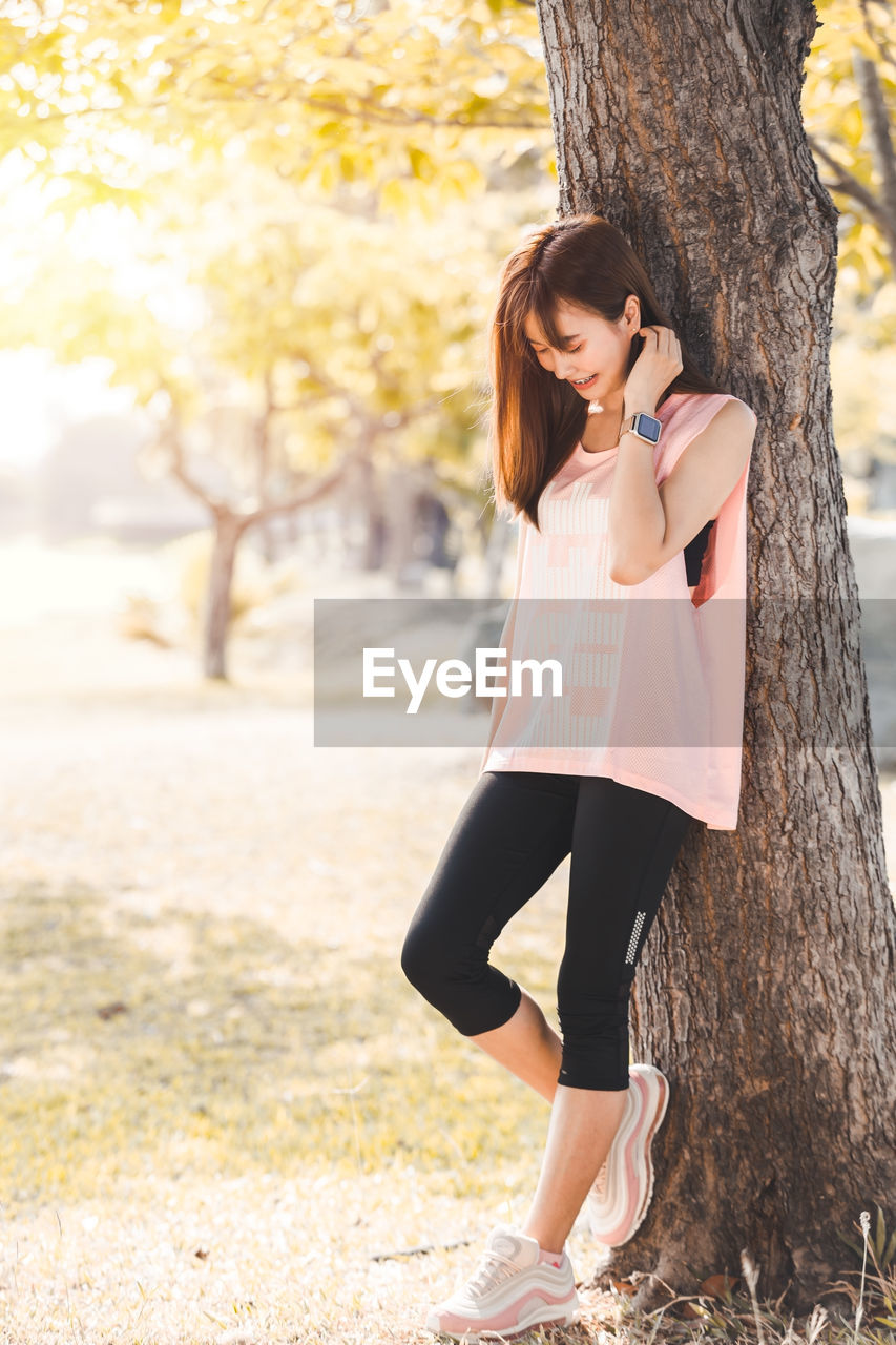 Full length of woman standing against tree trunk