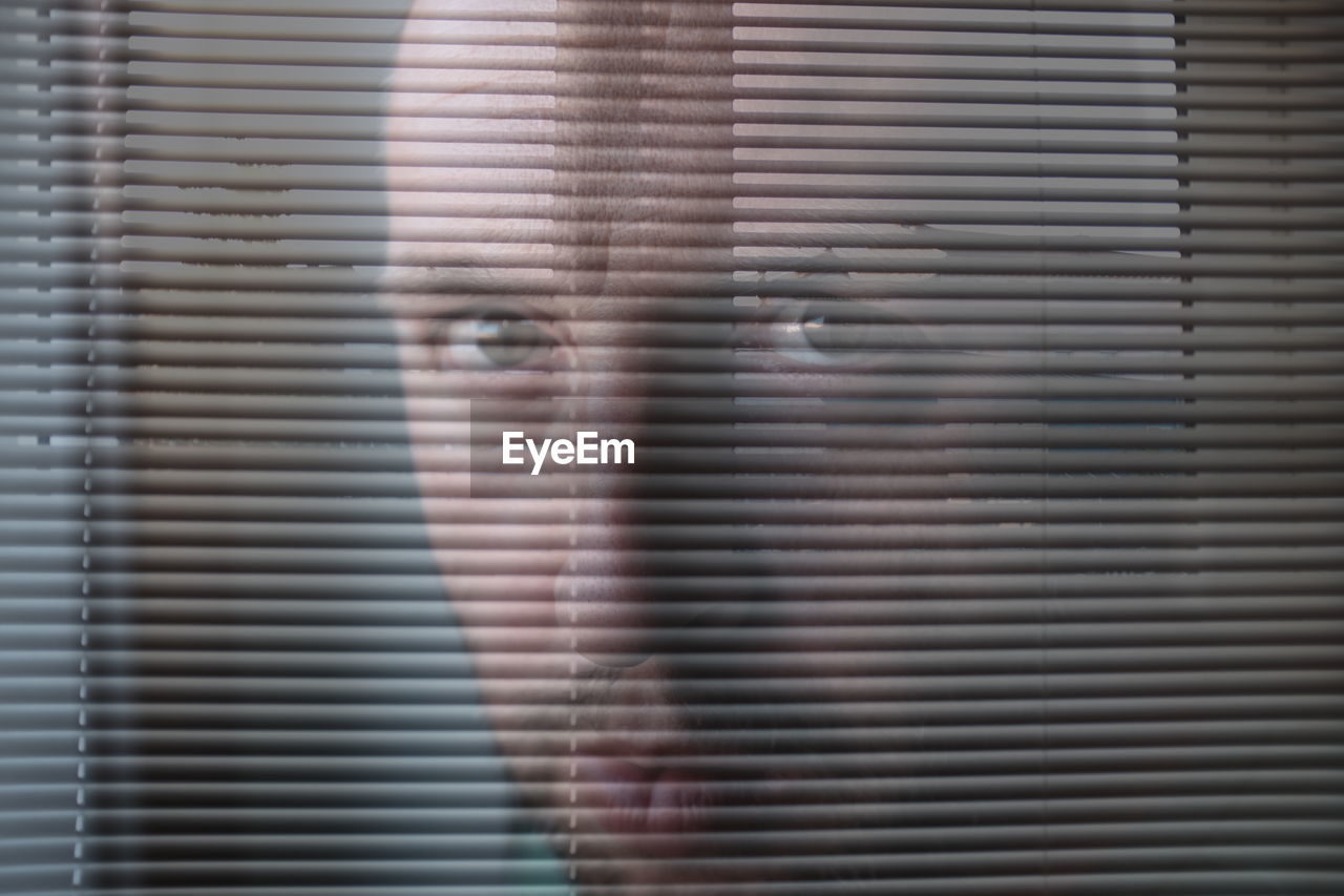 Portrait of angry man looking through window blinds