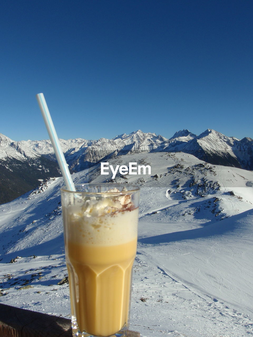 Close-up of drink on retaining wall against snowcapped mountains