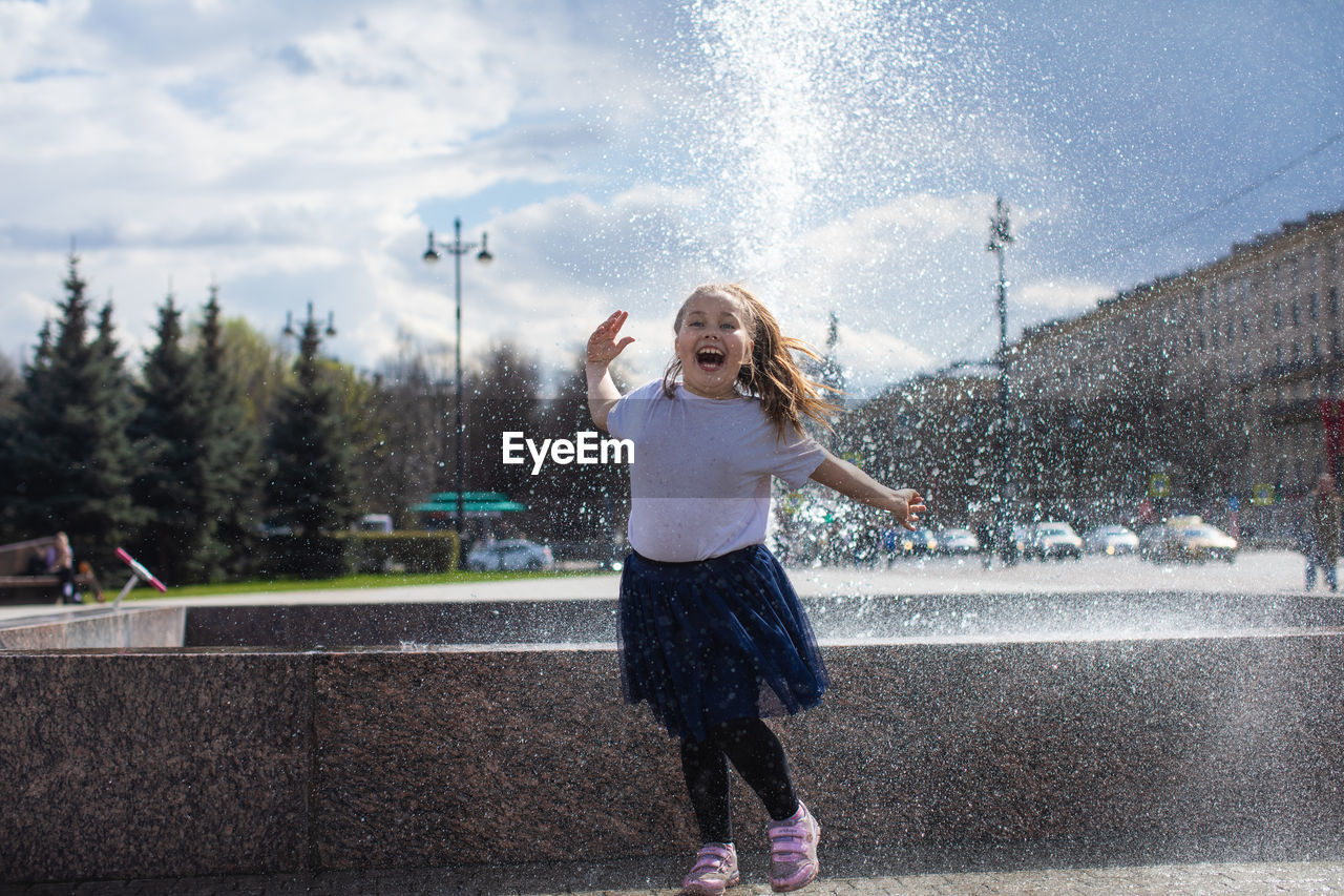 Happy little cute girl having fun in splashes a fountain