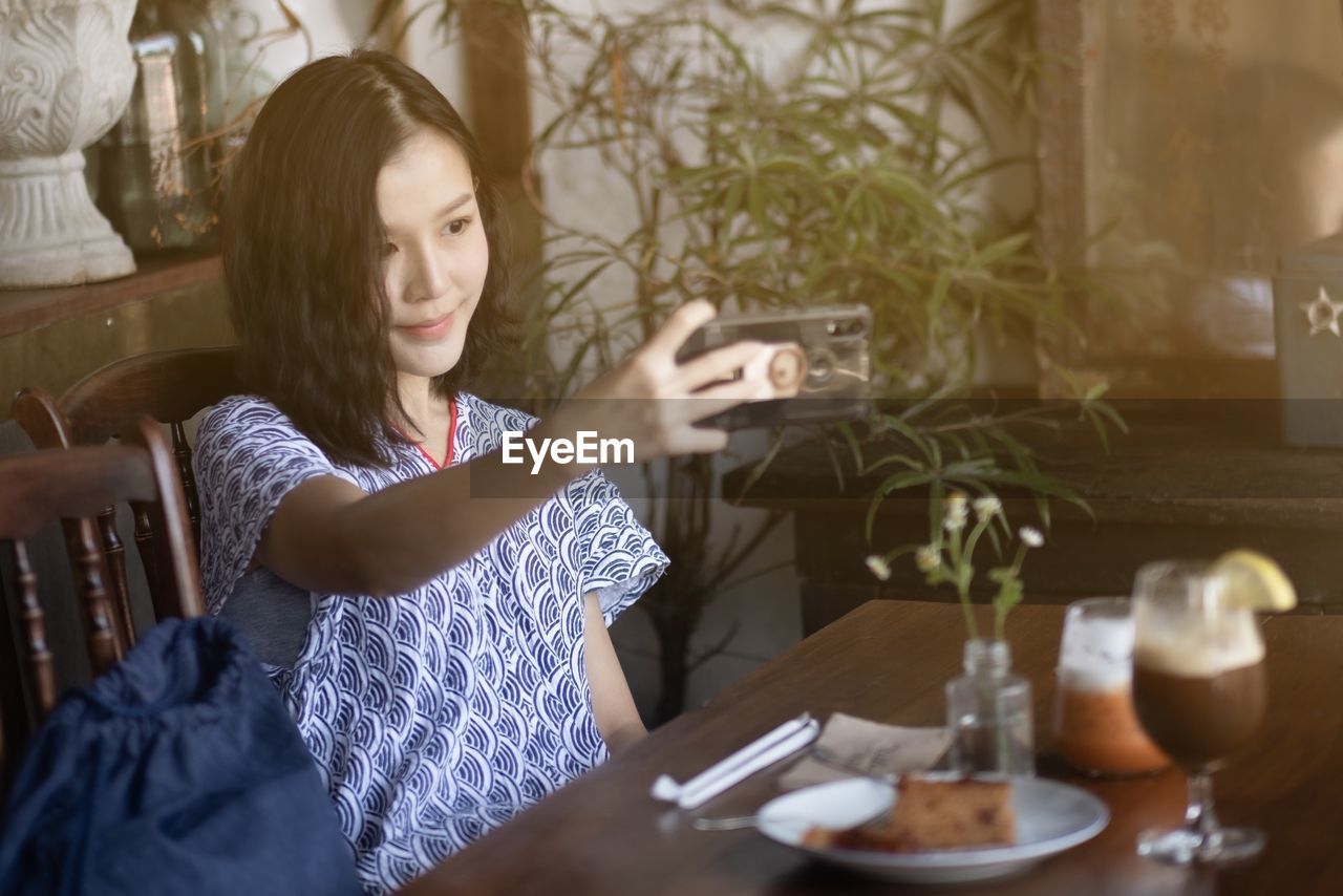 Smiling woman taking selfie while sitting at restaurant