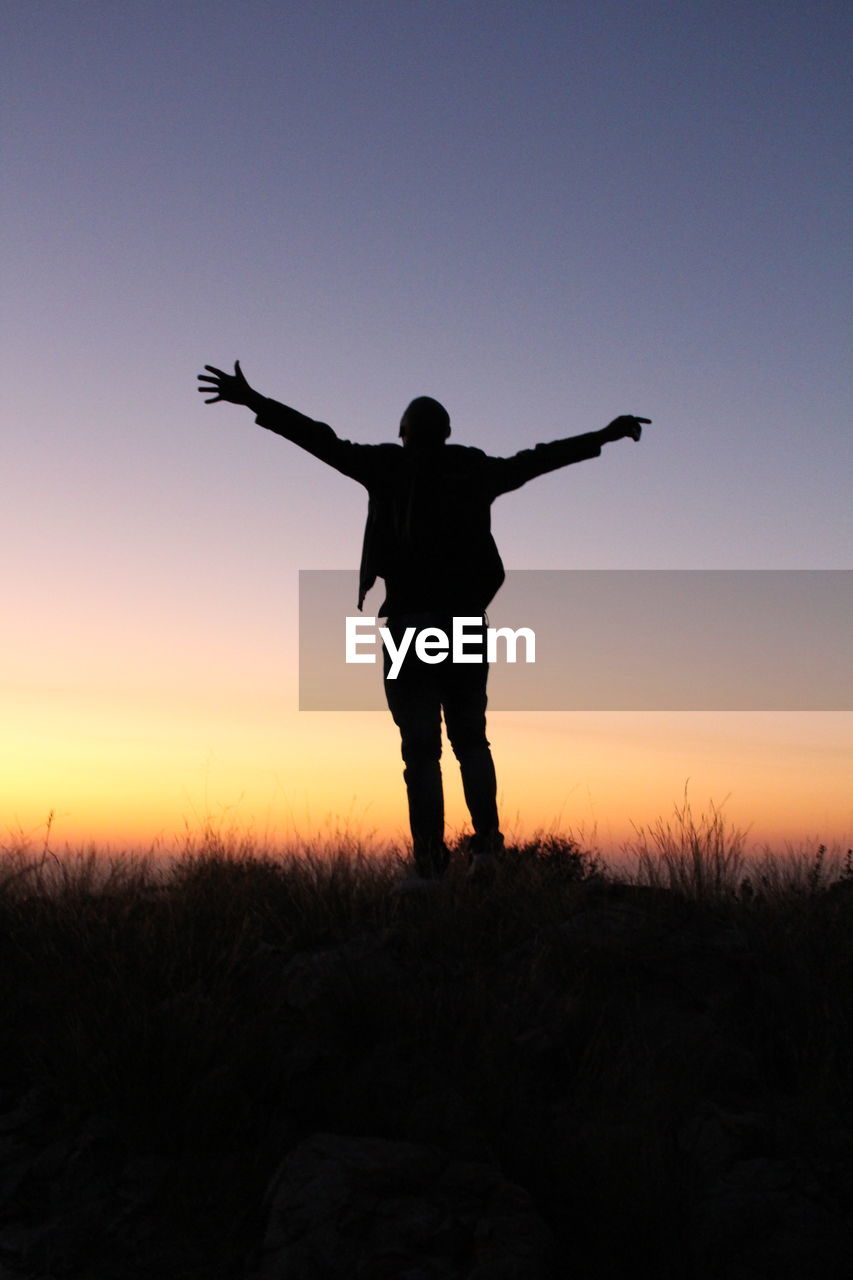 Silhouette man standing with arms outstretched against sky