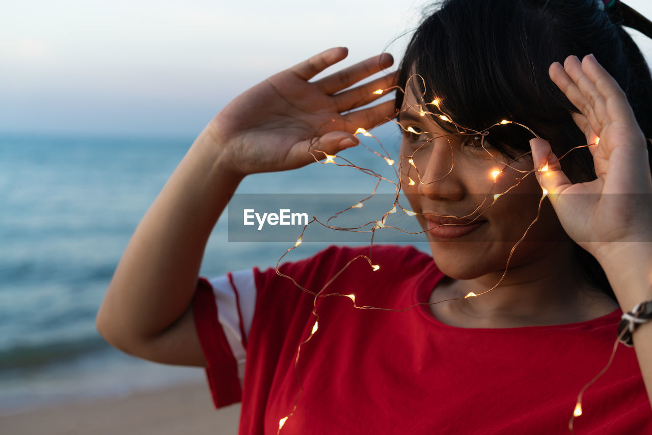 Woman with illuminated string lights looking away at beach