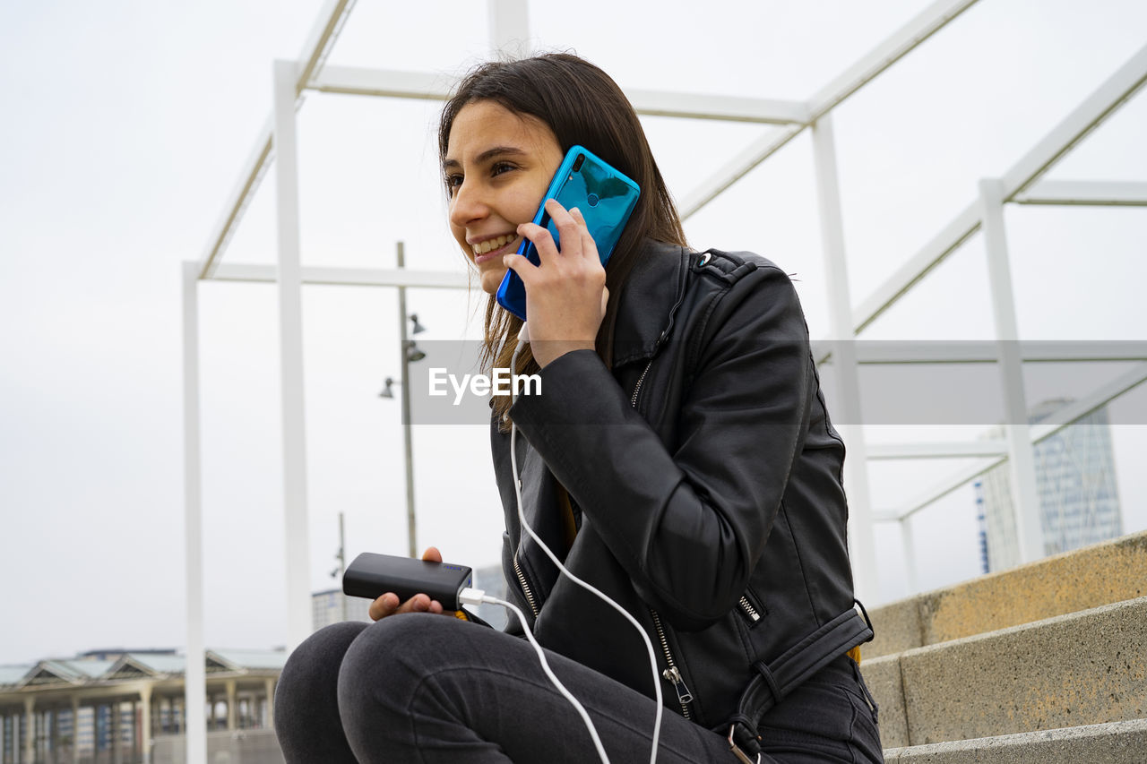 Woman talking on the phone while charging her mobile with a powerbank.